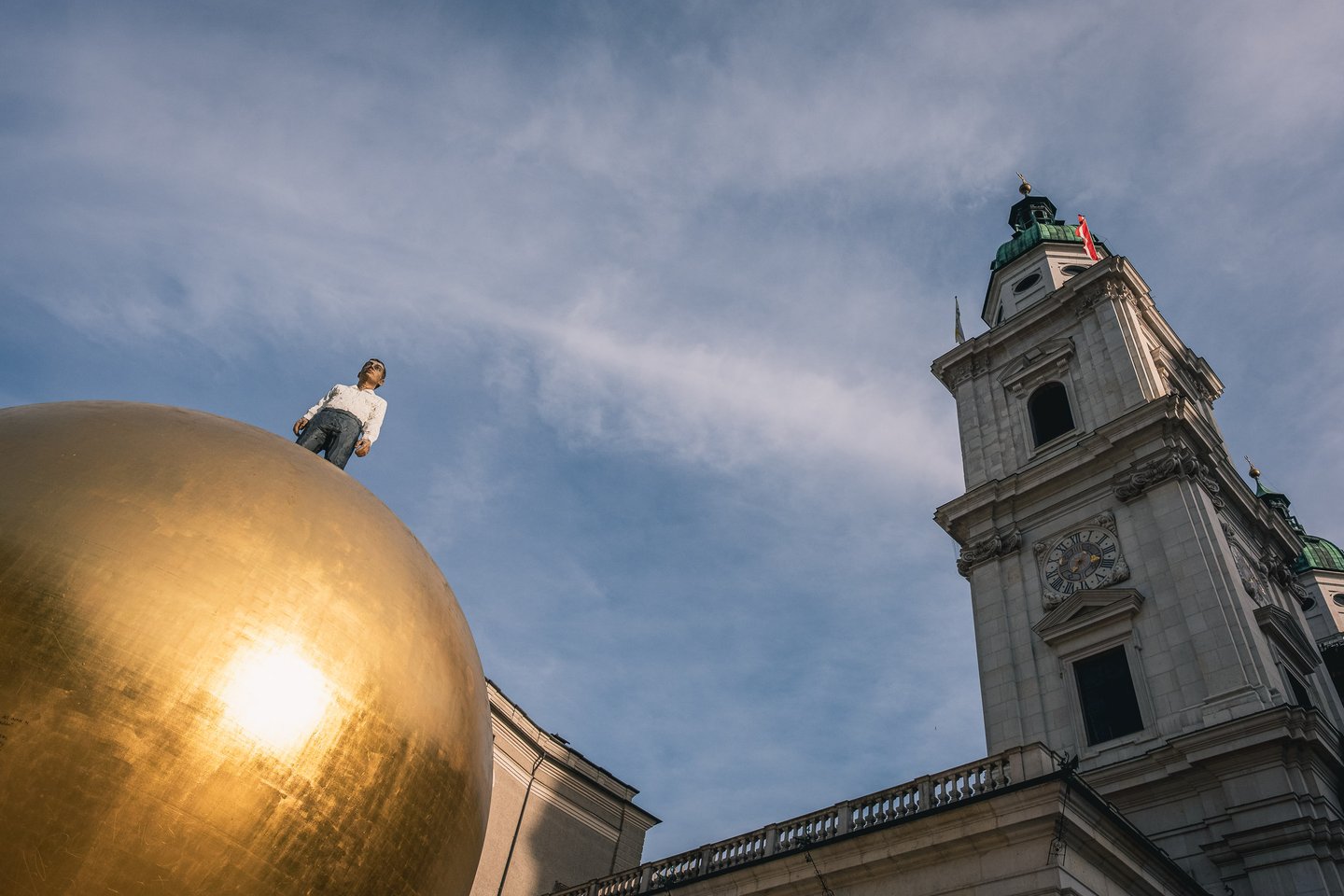 Man atop Sphaera golden ball sculpture beside Salzburg Cathedral tower in Salzburg old town