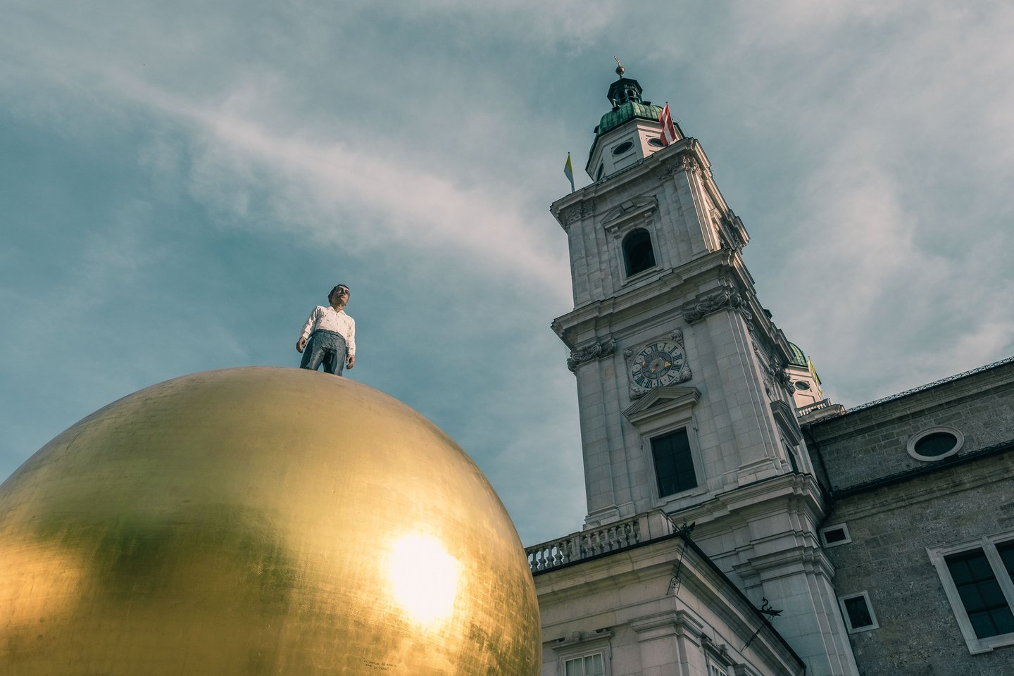 Figure standing on Sphaera sculpture with Salzburg Cathedral clock tower in Salzburg