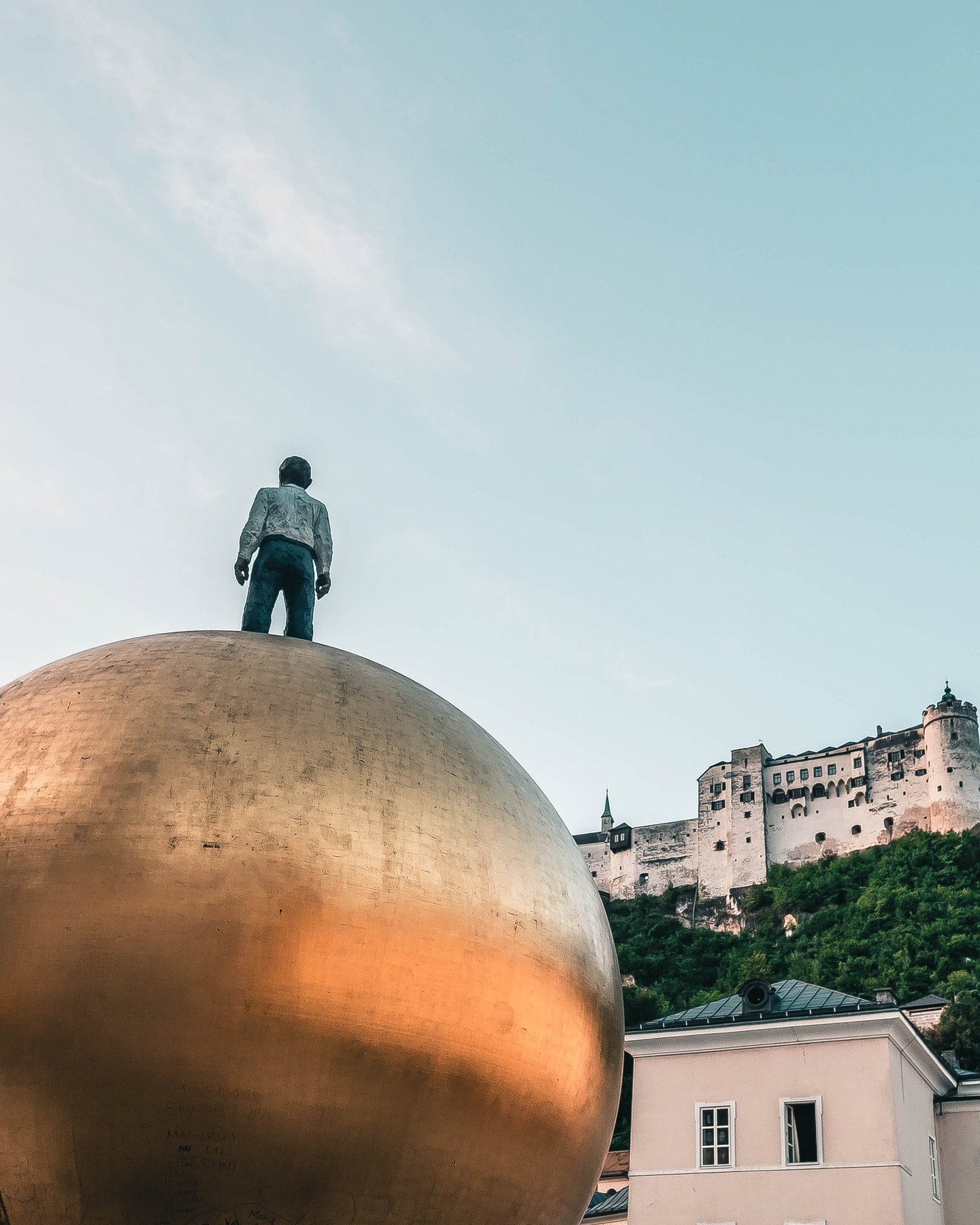 The Sphaera sculpture figure stands atop a golden ball with Hohensalzburg Fortress above in Salzburg.