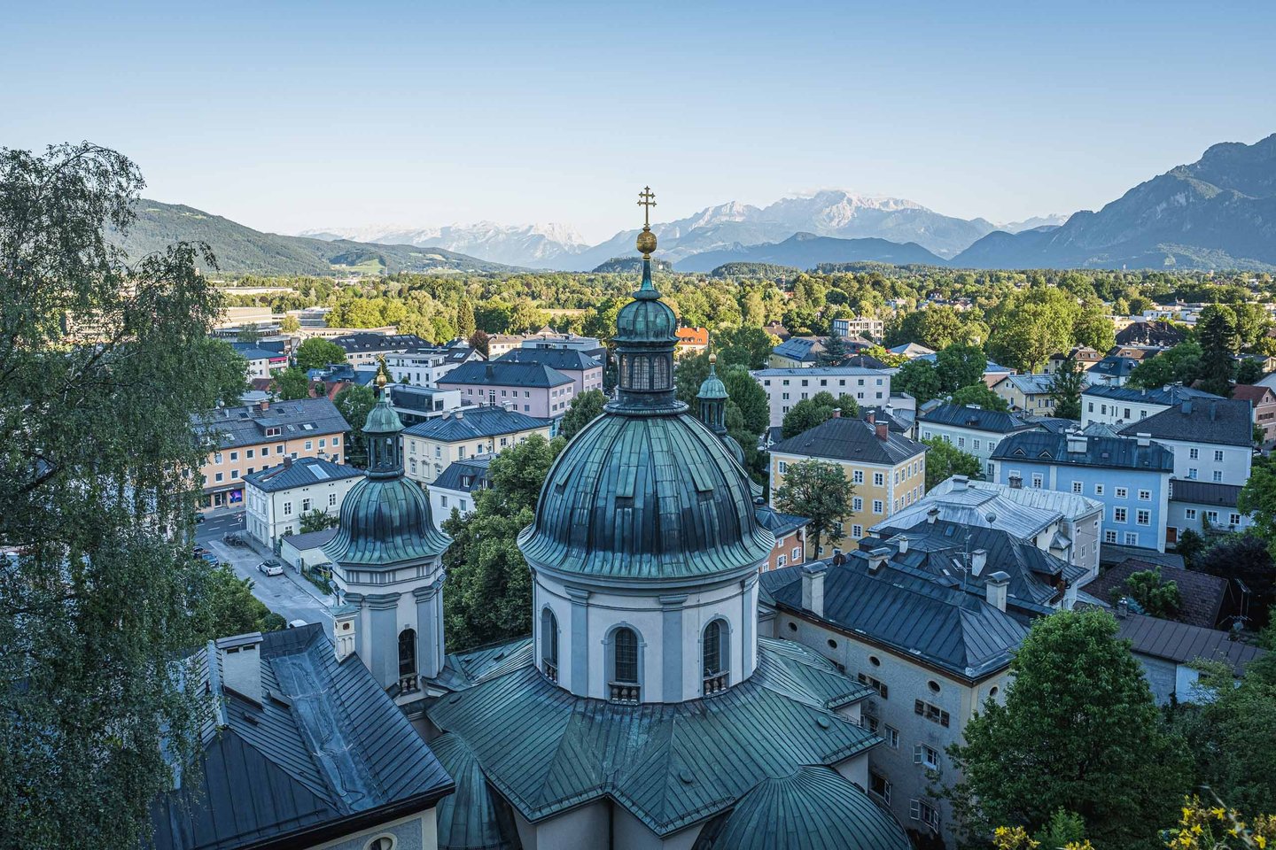Green-domed baroque church with rooftops and the Alps behind in Salzburg.
