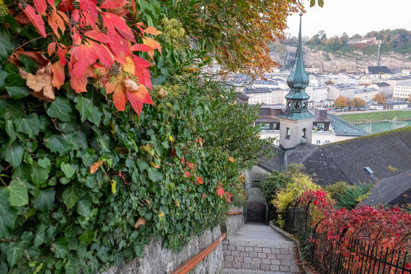 Onion-dome spire of St Johns church on Imberg seen from leafy pathway above Salzburg old town