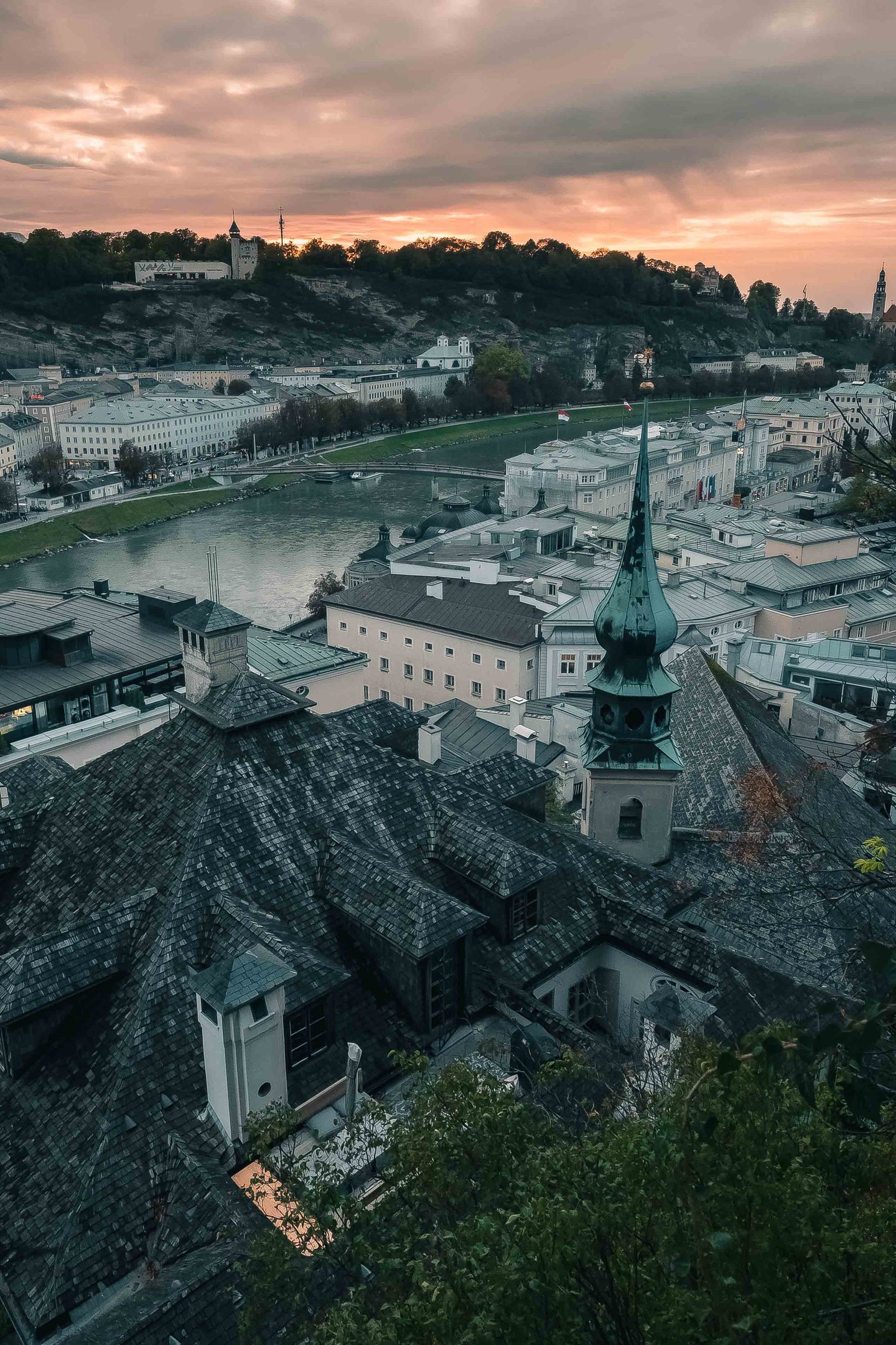 Slim green-copper spire of the Johanneskirche at Imbergstiege Kapuzinerberg rising above Salzburg Altstadt rooftops at dusk