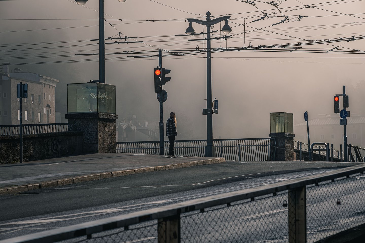 Pedestrian standing at red traffic light on Staatsbrücke in heavy morning fog over the Salzach in Salzburg