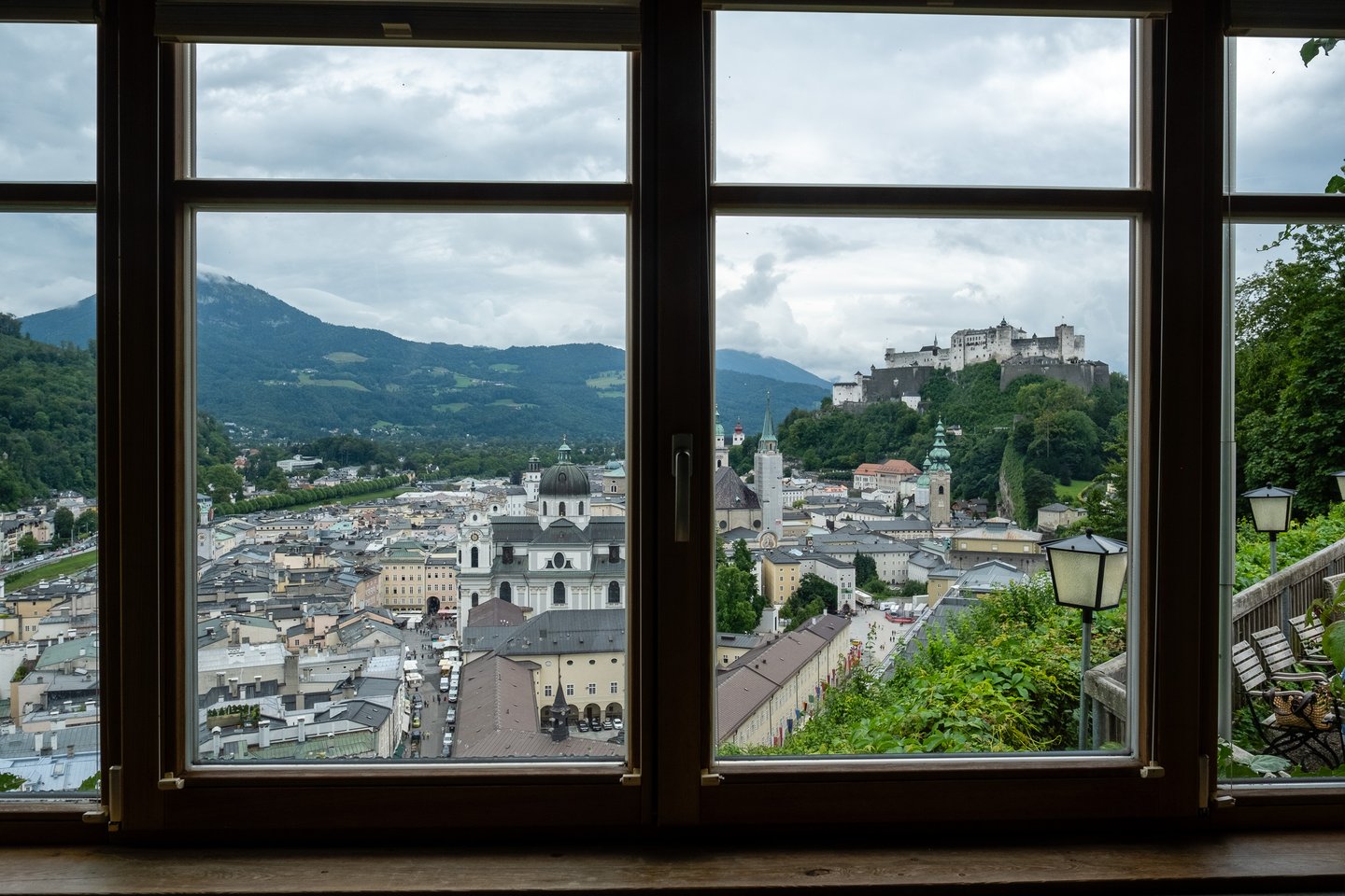 The Salzburg Altstadt seen through a wooden window of the Stadtalm on the Mönchsberg, with the Kollegienkirche and the market stalls on Universitätsplatz below, the Franziskanerkirche tower in the middle and Hohensalzburg on its rock to the right.