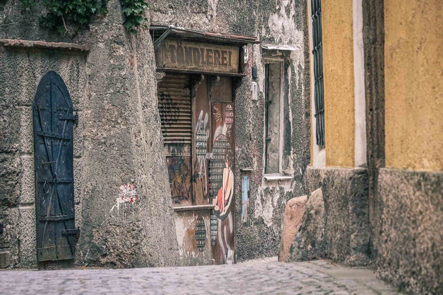 Weathered shop facade with a faded Tandlerei sign and worn blue door on Steingasse in Salzburg old town.