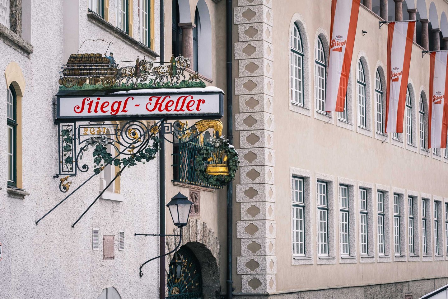 Ornate Stiegl-Keller wrought iron sign with painted horse-drawn beer cart above the entrance in Salzburg.