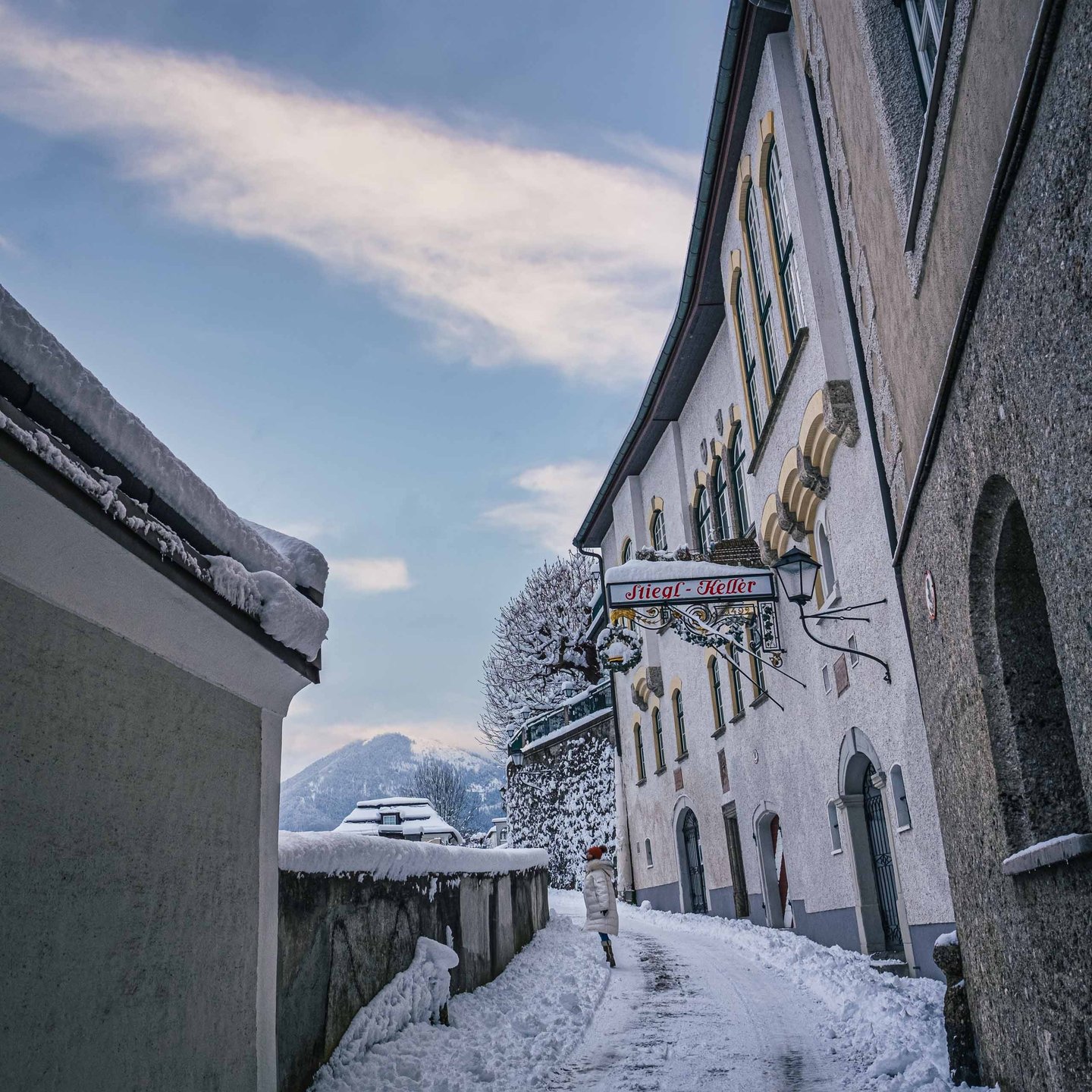 Edited snowy Festungsgasse view with Stieglkeller entrance and walker in Salzburg old town.