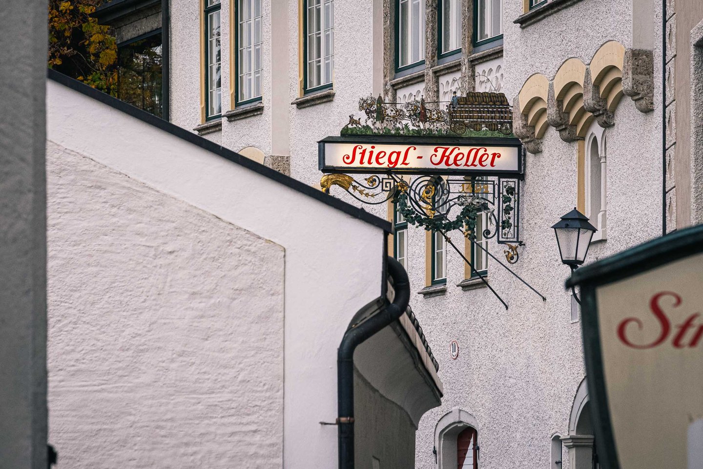 Ornate wrought iron Stiegl-Keller sign with golden horn hanging above a Salzburg alleyway.