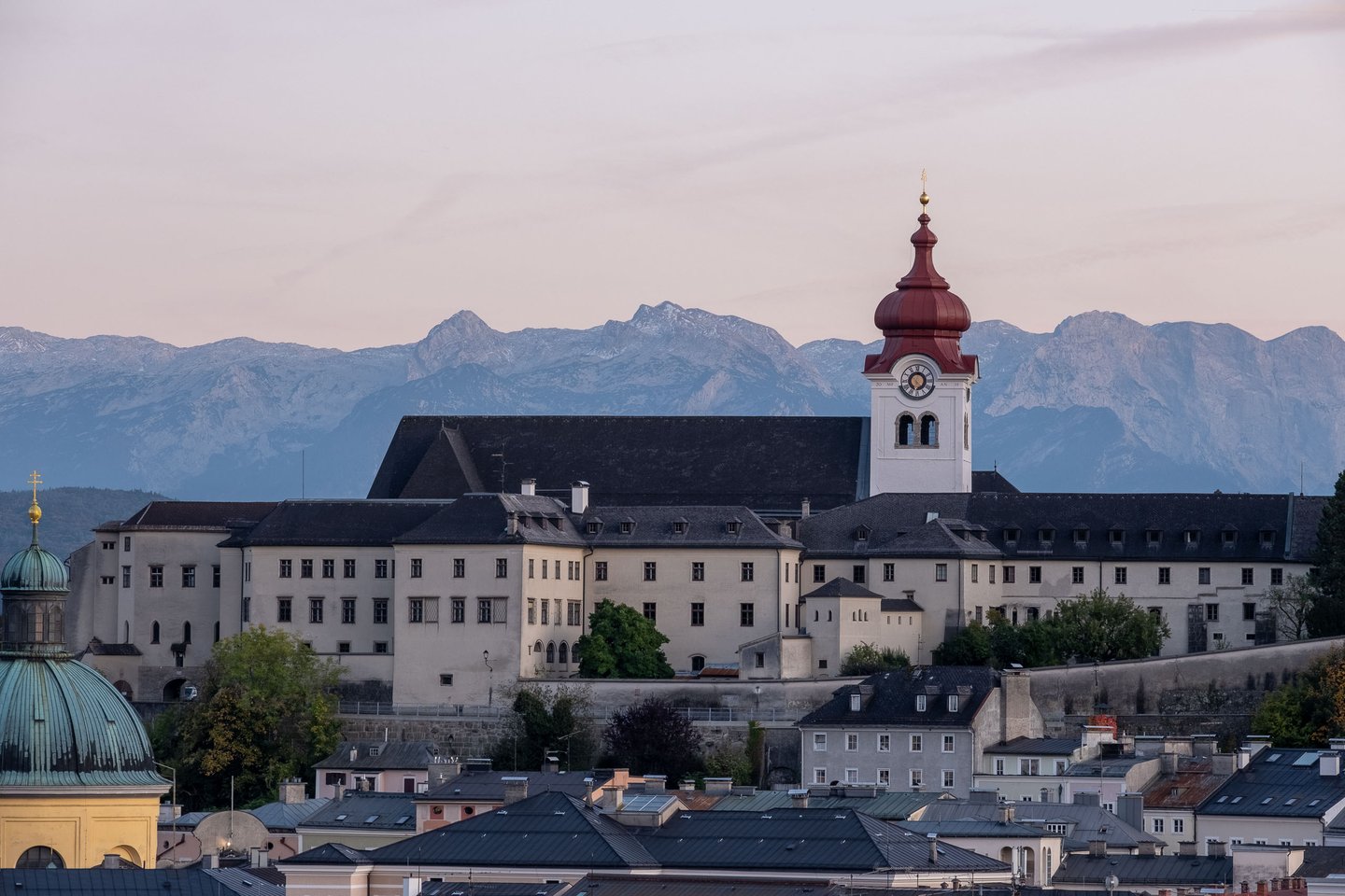 Nonnberg Abbey complex with its distinctive red-capped clock tower above Salzburg rooftops and the northern Alps beyond