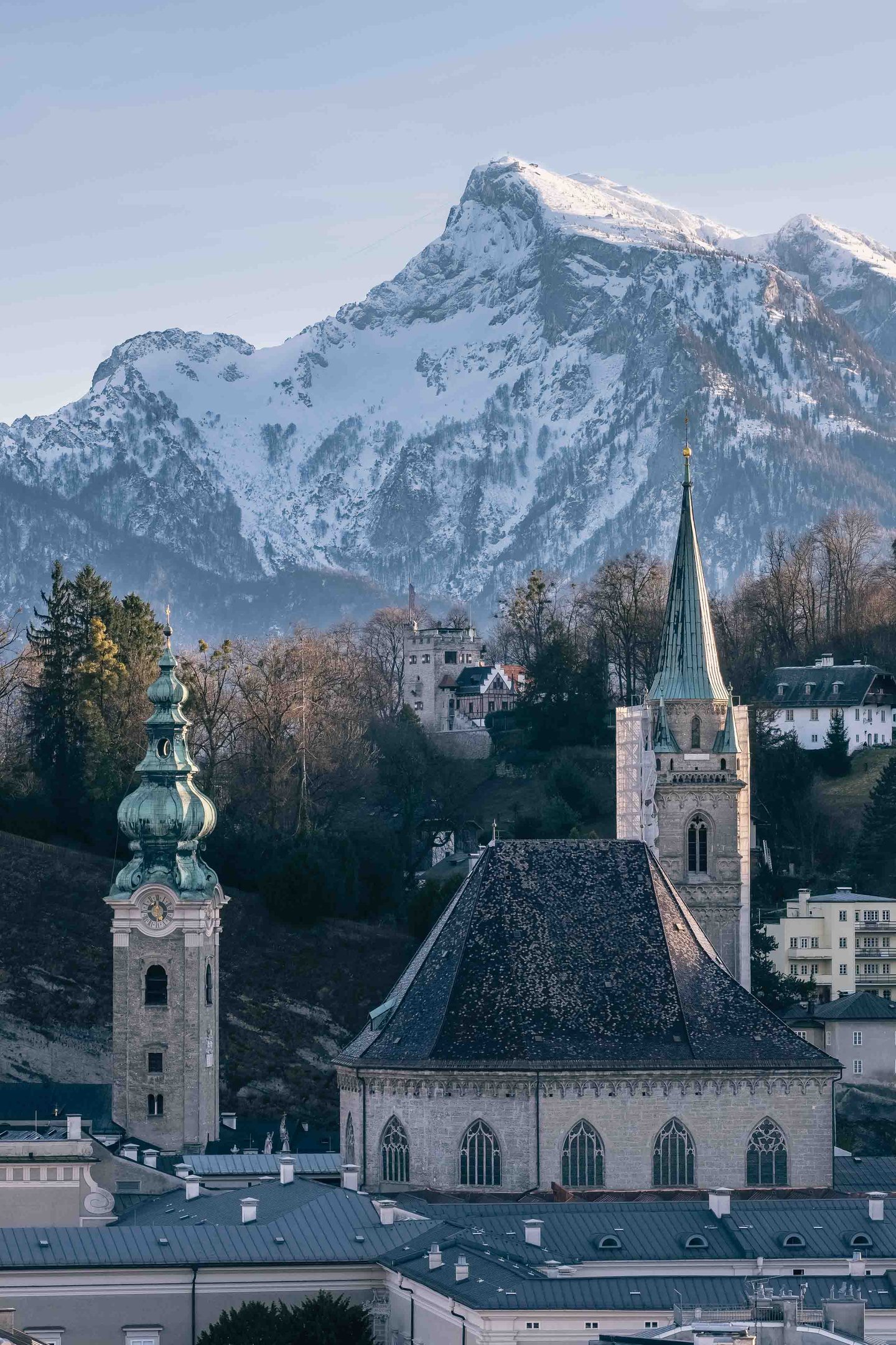 St Peter Abbey tower and Franziskanerkirche spire rise above old town rooftops with Untersberg behind in Salzburg.