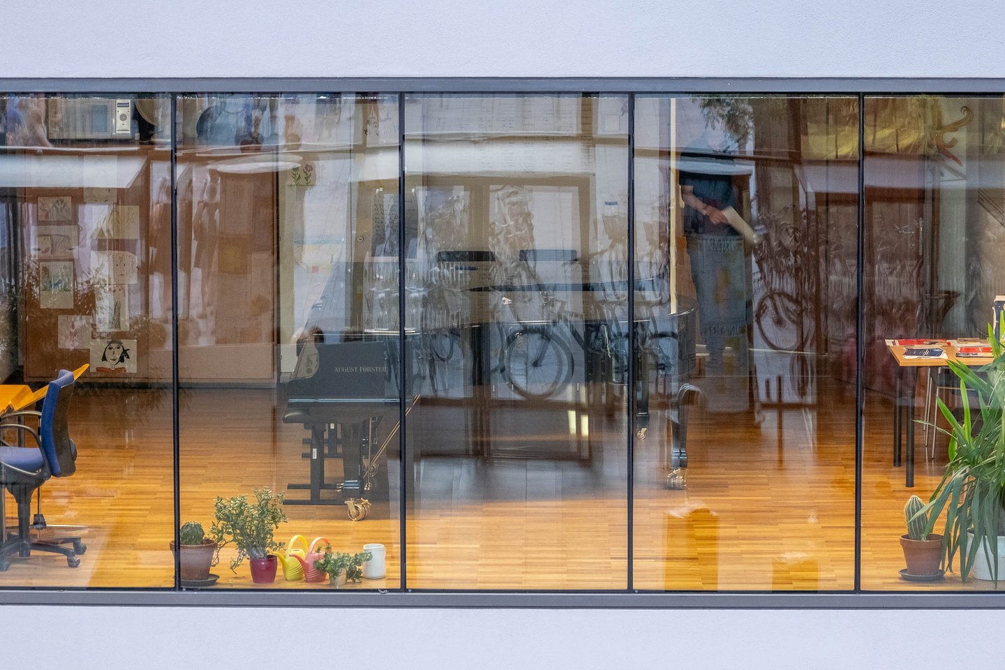 Grand piano and bicycle visible through the glass facade of a ground-floor studio at the Universitaet Mozarteum building in Salzburg-Mirabellplatz