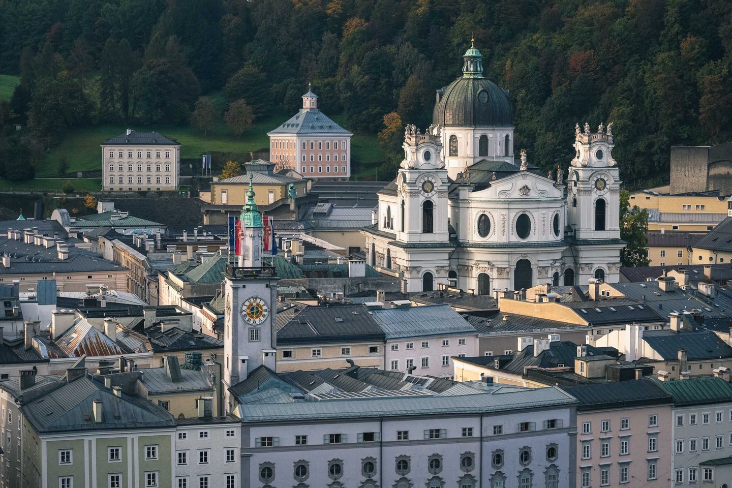 Kollegienkirche twin-towered facade and dome with Neue Residenz clock tower rising above Altstadt rooftops in Salzburg.