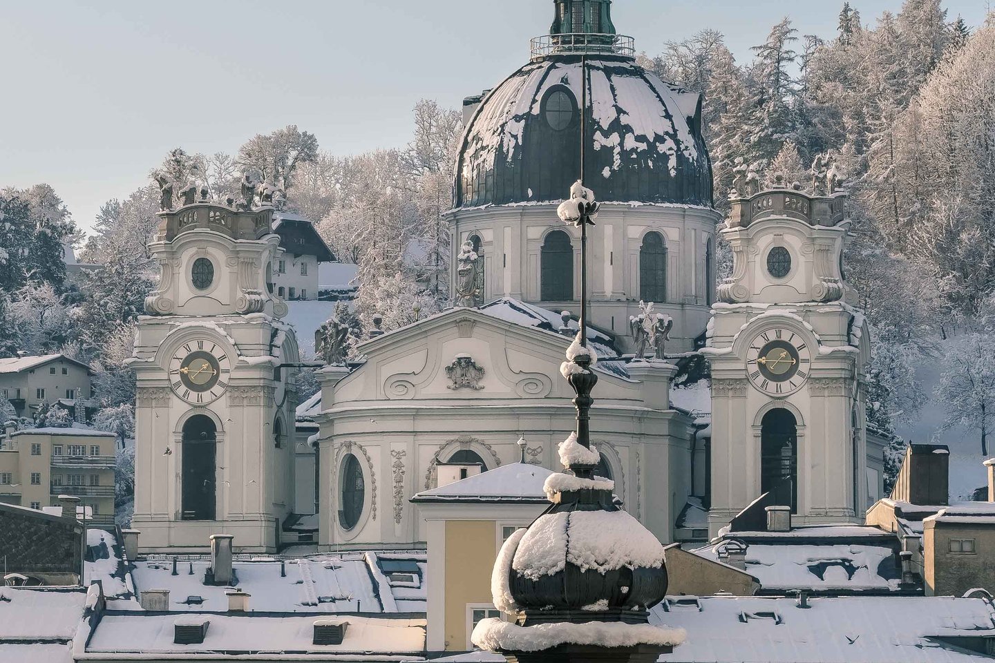 Snowy baroque dome and twin towers of Kollegienkirche above Salzburg old town rooftops.
