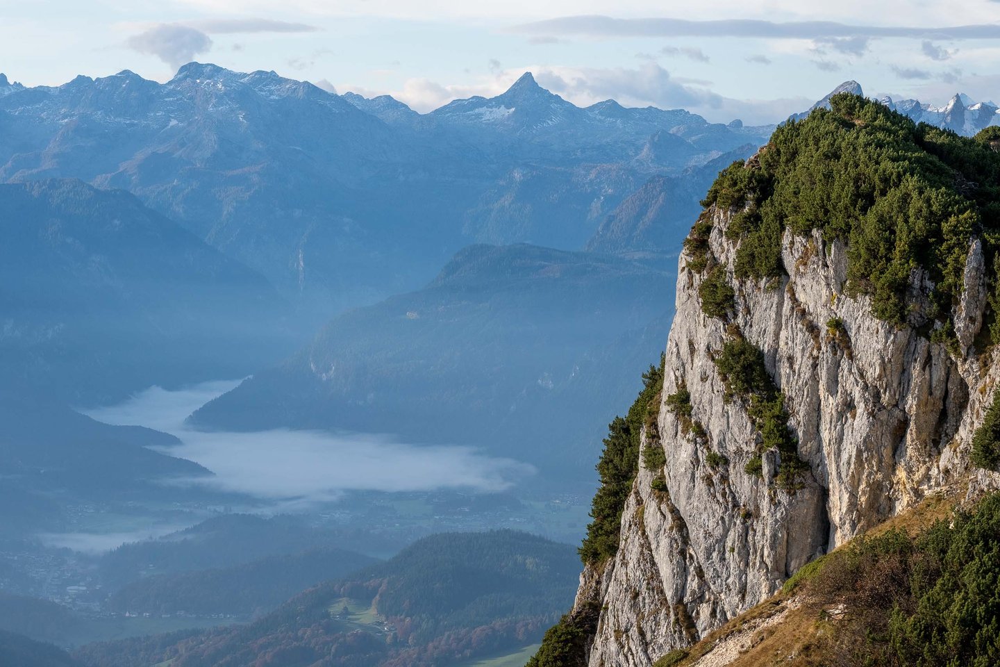 Steep cliffs of the Untersberg drop toward the misty Koenigssee valley at dawn in Berchtesgaden.