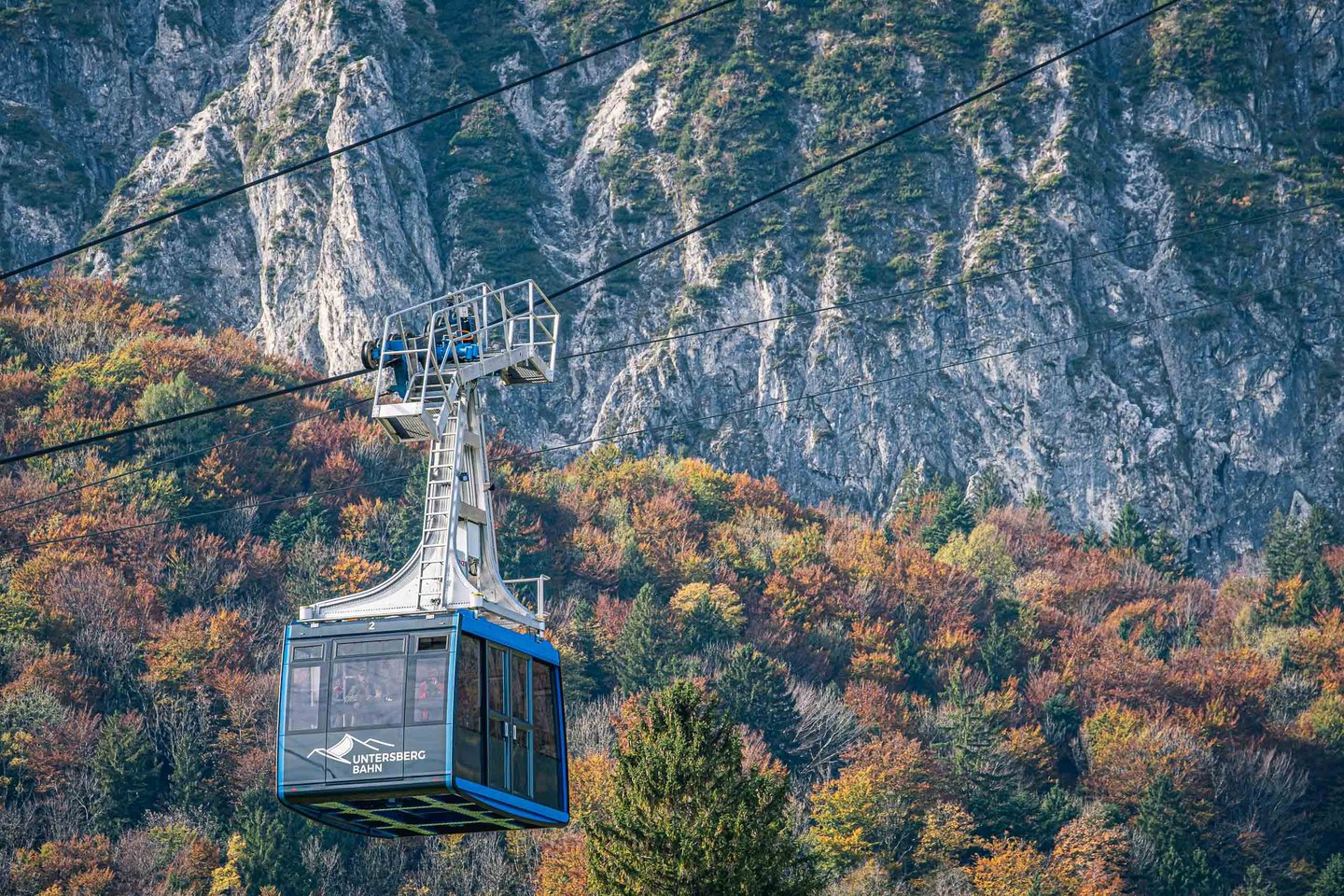 Untersbergbahn cable car cabin rising against limestone cliffs above autumn forest near Grodig