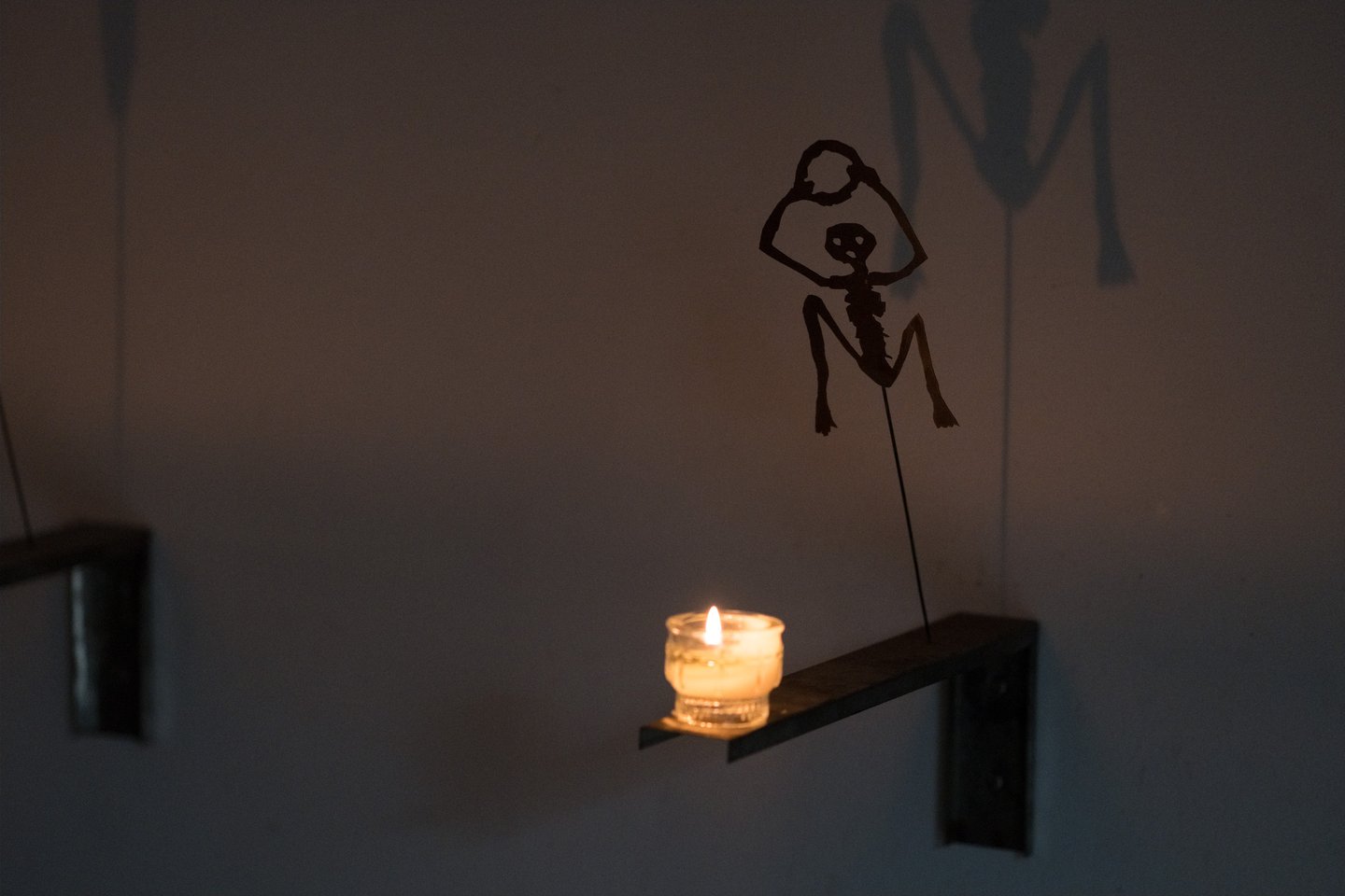 A single candle on a small wall bracket throws the enlarged shadow of a cut-metal skeleton figure across the wall of the crypt beneath Salzburg Cathedral.