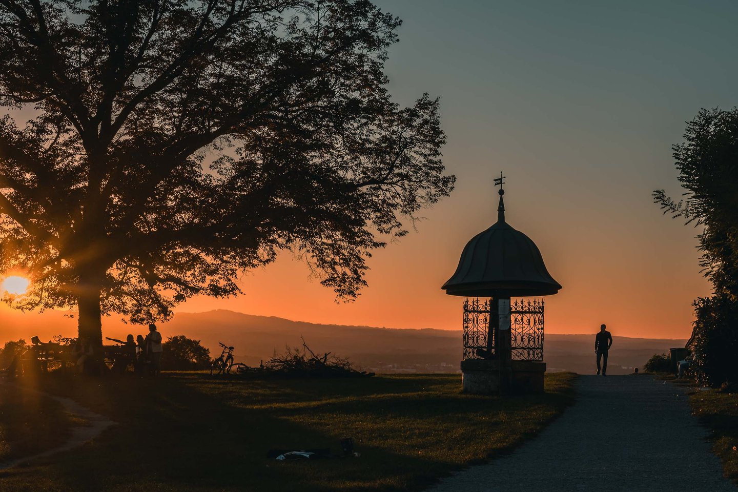 Iron wayside shrine silhouetted against orange sunset sky at Maria Plain near Salzburg