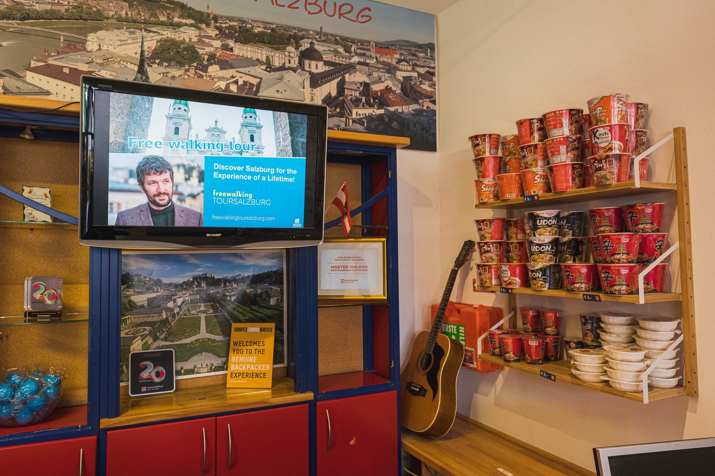 Reception area of the YoHo hostel in Salzburg with walking tour screen and instant noodle shelf.