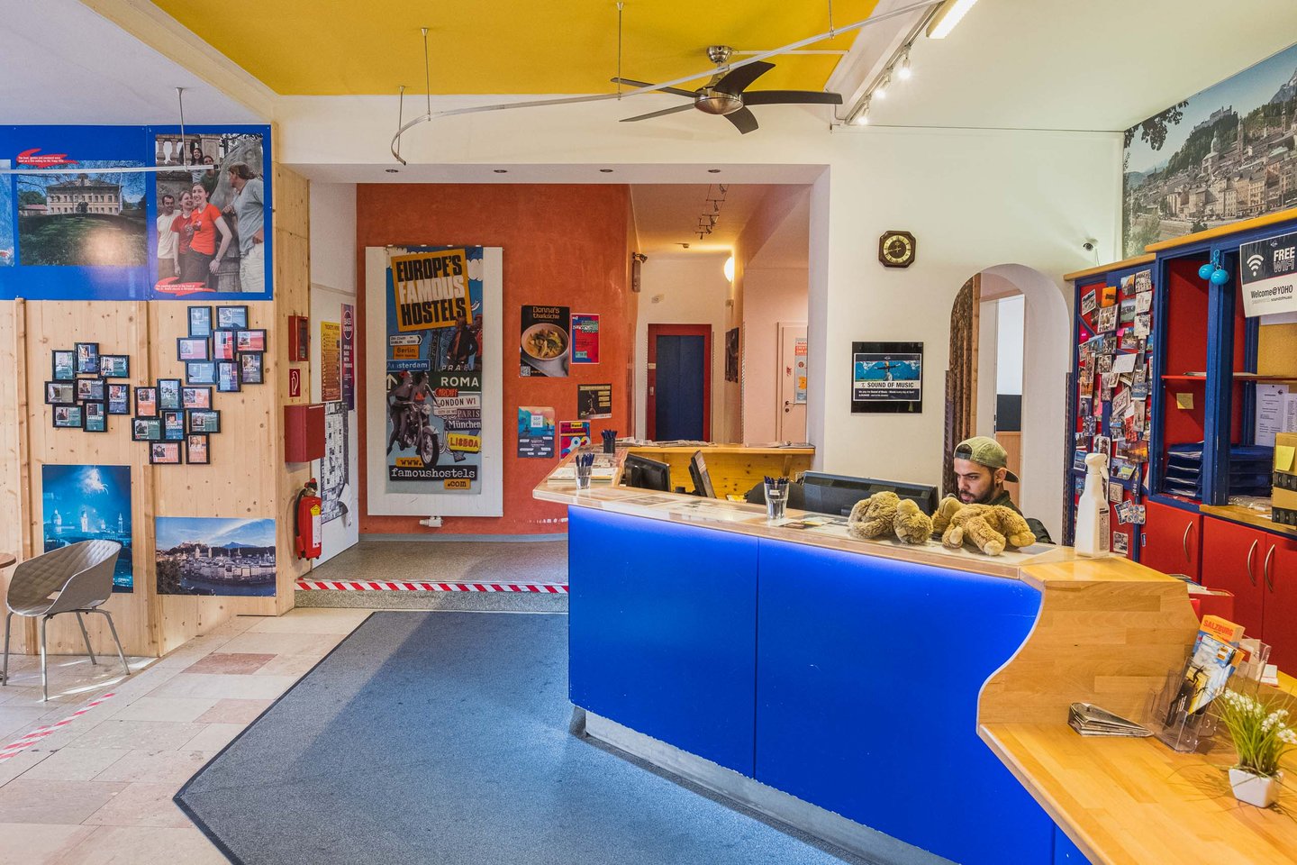 Colourful reception desk with a staff member and travel posters inside YoHo Hostel in Salzburg