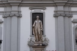 The stone statue of Joseph Haydn holding a quill and a sheet of music, standing on its pedestal in front of the pilastered facade of the Mariahilfer Kirche in Vienna.