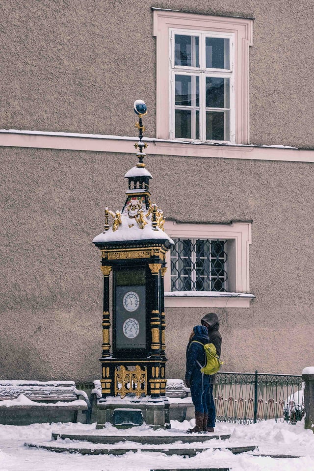 Ornate Jugendstil weather column (Wettersaeule) with gilded ornamentation on Alter Markt in Salzburg in winter snow