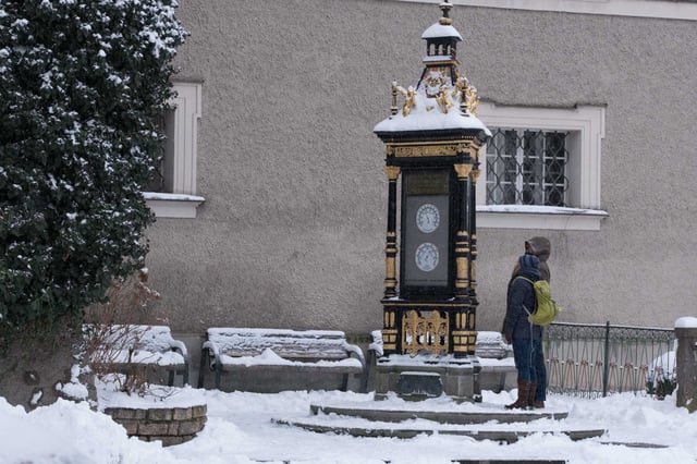 Person standing next to the Jugendstil Wettersaeule on Alter Markt in Salzburg in winter snow
