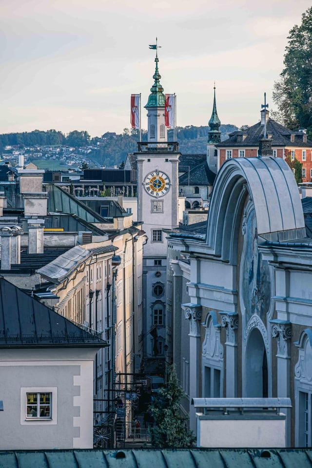 Altes Rathaus clock tower with Austrian flags next to the Festspielhaus facade in Salzburg old town.
