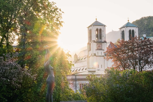 Sunrise light behind a figurative sculpture with the Andraekirche towers in Salzburg Neustadt.