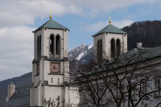 Twin towers with green pavilion roofs and gold crosses on the Andrakirche in Salzburg with the snowy Gaisberg behind