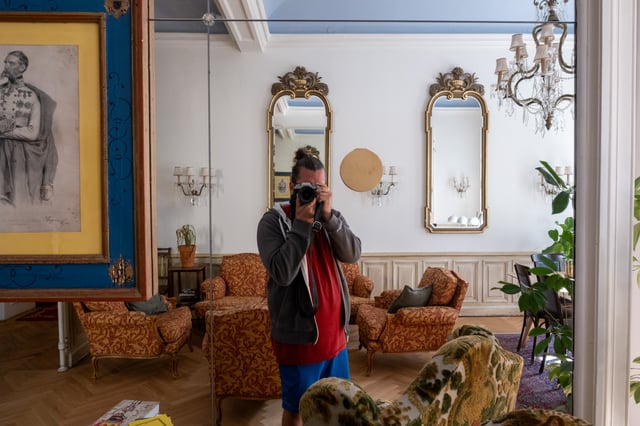 The photographer photographs his own reflection in the mirrored wall of a hotel salon in Bad Gastein, surrounded by gilt mirrors, crystal chandeliers and brocade armchairs.