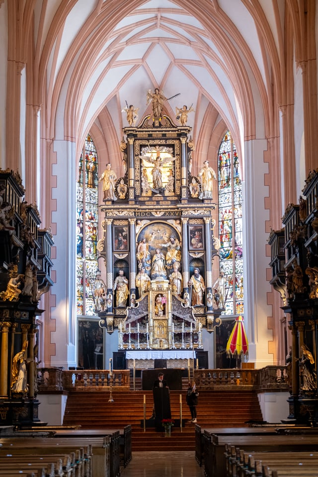 The black and gold high altar of Mondsee Basilica rises under salmon-pink Gothic rib vaulting, flanked by tall stained glass windows.