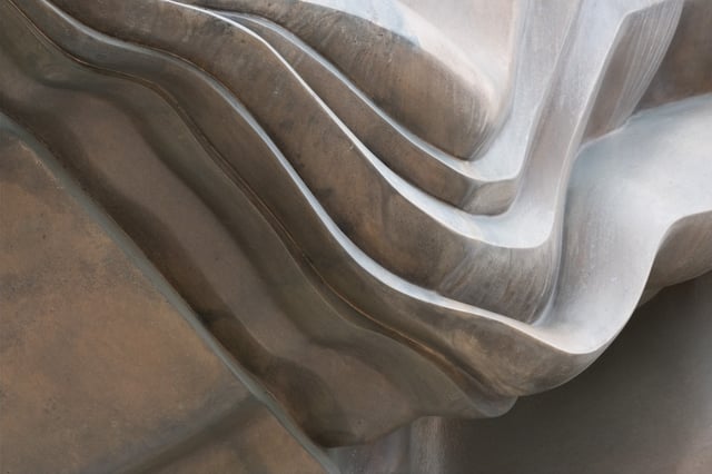 A close detail of the sculpture Caldera on Makartplatz in Salzburg, showing its stacked wave-like folds banded in brown and pale grey.