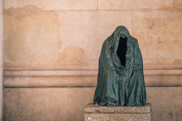 Bronze hooded cloak sculpture (Mantel des Gewissens / Cloak of Conscience) by Anna Chromy with empty interior set against a stone wall in Salzburg