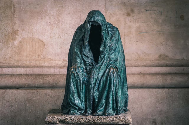 Hooded bronze seated figure (Cloak of Conscience by Anna Chromy) under the cathedral arcade in Salzburg old town