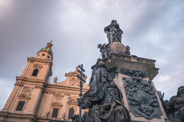 Mariensaeule Marian column silhouetted against the Salzburg Cathedral facade at dusk in Salzburg.