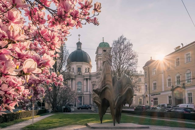 Magnolia in full bloom and bronze sculpture with Dreifaltigkeitskirche domes and sun flare in Salzburg.