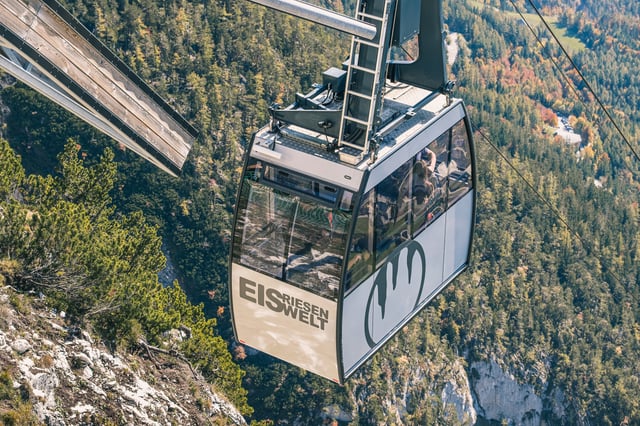A gondola of the Eisriesenwelt cable car, lettered EIS RIESEN WELT with the ice-stalactite logo, hangs above autumn-coloured forest on the slope near Werfen.