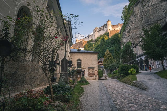 Cobblestone Festungsgasse climbing toward Hohensalzburg Fortress with shrines and greenery in Salzburg old town