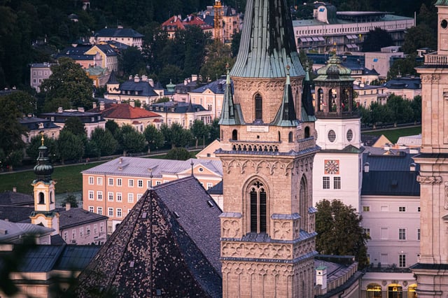 Gothic tower of Franziskanerkirche with green roof and pyramid cap rising above Salzburg old town rooftops