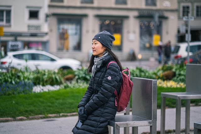 Close portrait of the guide in a grey beanie and red backpack, perched against one of the steel Spirit of Mozart chairs and looking away to her right.