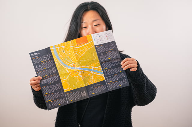 A smiling woman holds open the printed Free Walking Tour Salzburg city map, its yellow street plan of the old town flanked by illustrated landmark notes.