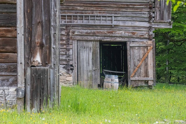 Weathered wooden barn with open doorway and barrel in a meadow at the open-air museum near Salzburg.