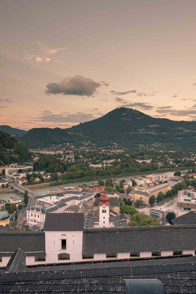 View across Salzburg rooftops toward Gaisberg with a white onion-dome church in the foreground.