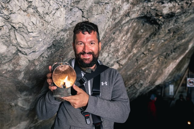 Gerhard Reus, bearded and in a grey hoodie, holds up a lit carbide lamp at the Eisriesenwelt cave entrance.