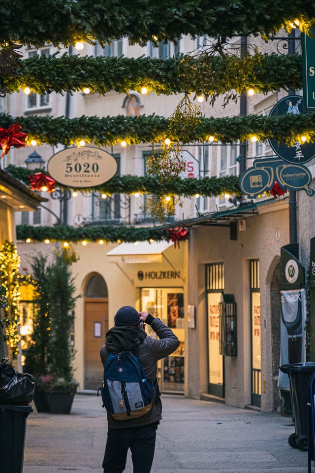 Photographer under Christmas garlands and guild signs in a decorated Salzburg old town alley.