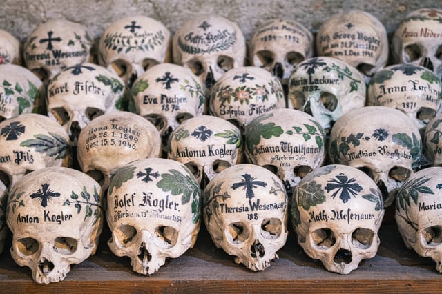 Rows of skulls painted with names, dates, crosses and leafy wreaths stacked on a wooden shelf in the Hallstatt bone house.