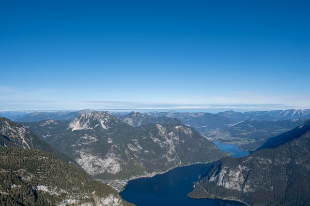 From high on the Krippenstein the Hallstaetter See runs away between steep wooded walls, with Hallstatt small on its left shore and the wide valley and further ranges beyond the far end.