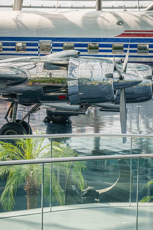 A Flying Bulls aircraft sits under the Hangar-7 glass dome beside palm trees in Salzburg.