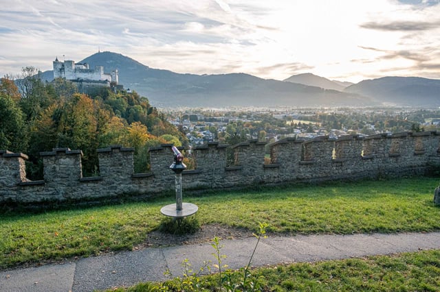 View from Hettwer Bastei battlements across Salzburg toward Hohensalzburg Fortress and Gaisberg at sunrise.