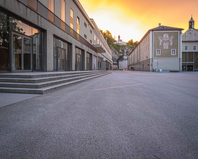 Empty Hofstallgasse with Festspielhaus facade and fortress hill at sunset in Salzburg old town.